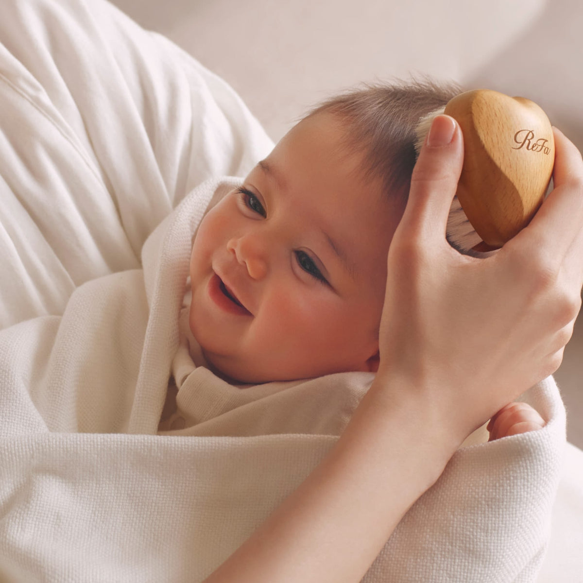 Hand brushing a smiling baby with the heart-shaped ReFa BABY SLEEPY Heart brush