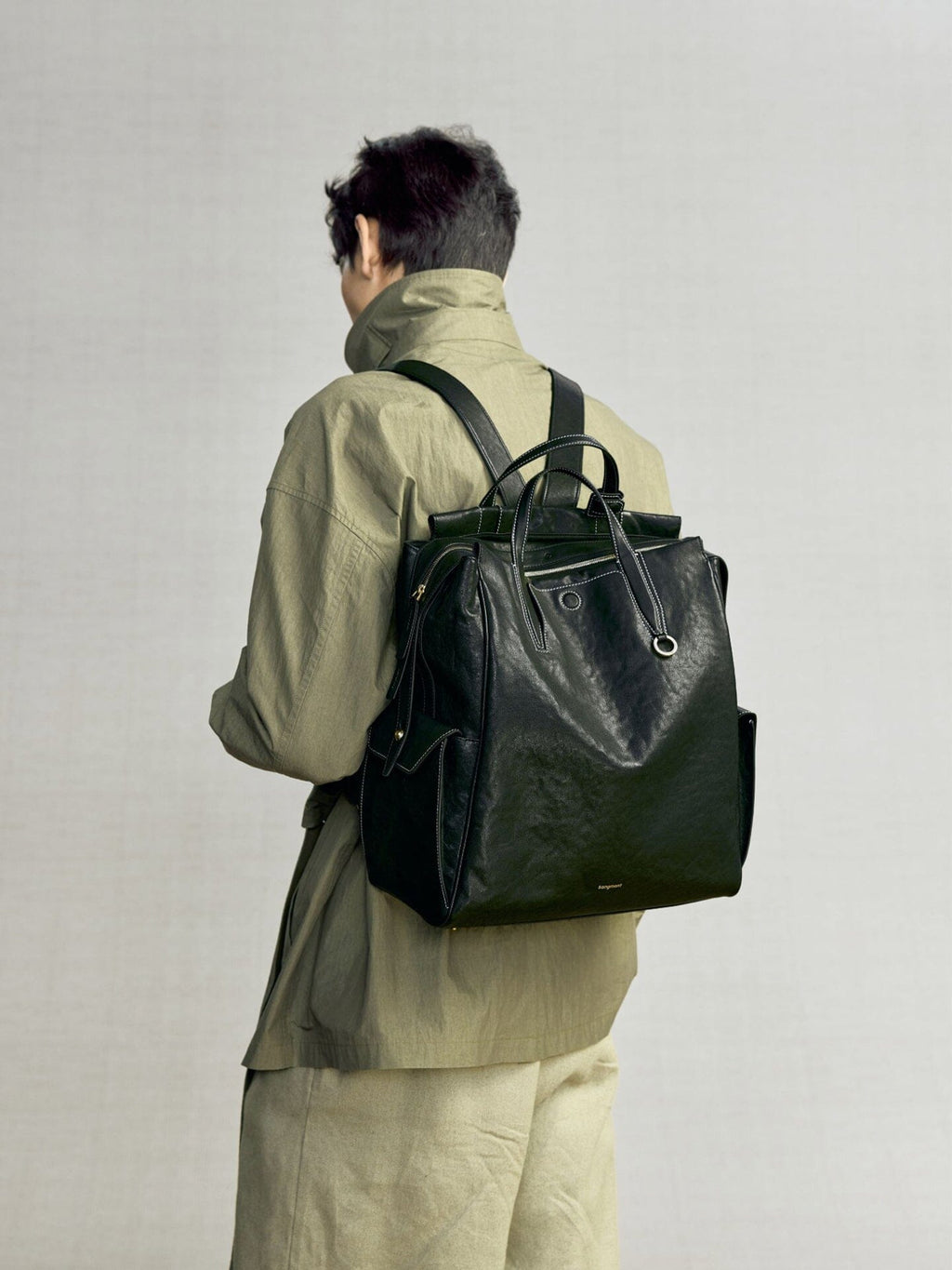 Songmont Large Yore Backpack Onyx - worn on the back over an olive jacket