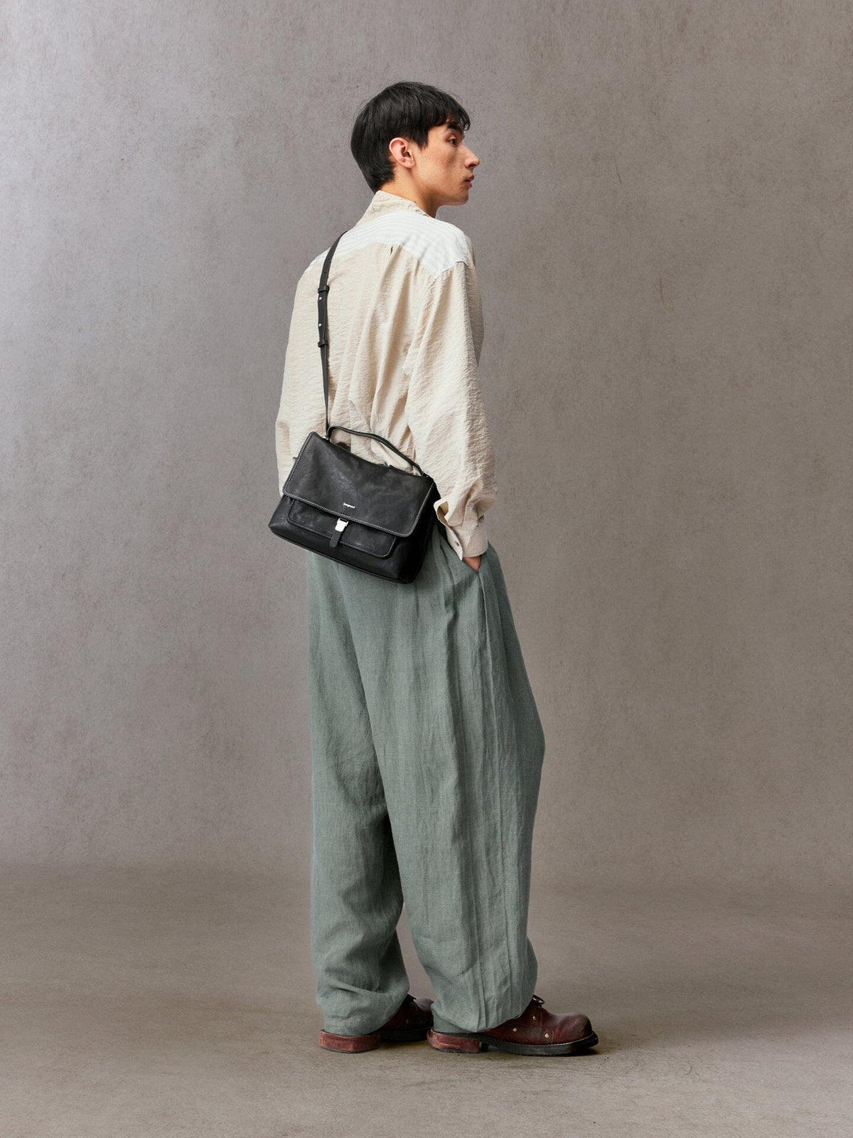 Songmont Small Shan Messenger Bag Onyx - worn across the body with a cream shirt and green trousers