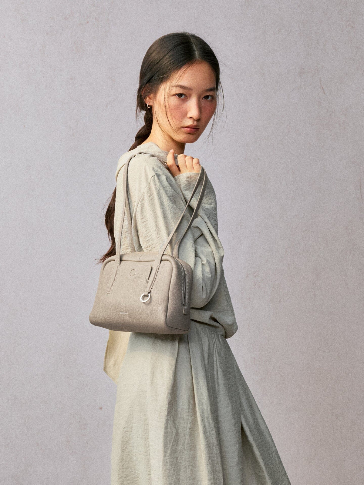 Songmont Small Yore Trunk Bag Smoke Grey - worn on the shoulder with a hand on the strap