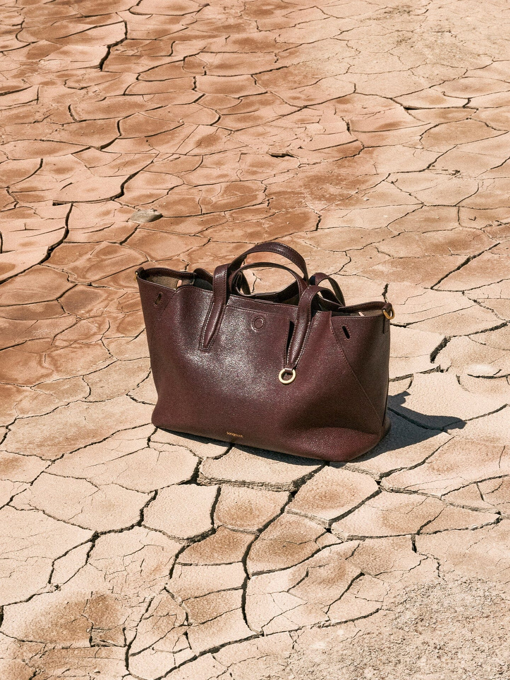 Songmont Small Yore Tote Bag Raisin - open tote resting on cracked dry earth