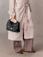 Songmont Small Shan Messenger Bag Onyx - carried by the top handle with a long blush coat