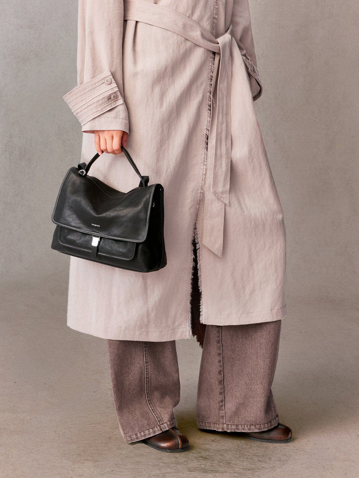 Songmont Small Shan Messenger Bag Onyx - carried by the top handle with a long blush coat