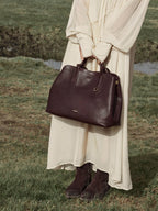 Songmont Large Yore Tote Bag Raisin - held in front with a cream dress