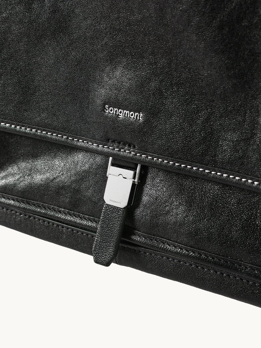 Songmont Small Shan Messenger Bag Onyx - close-up of the logo, contrast stitching and buckle tab