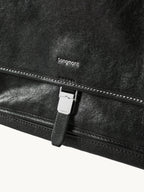 Songmont Small Shan Messenger Bag Onyx - close-up of the logo, contrast stitching and buckle tab