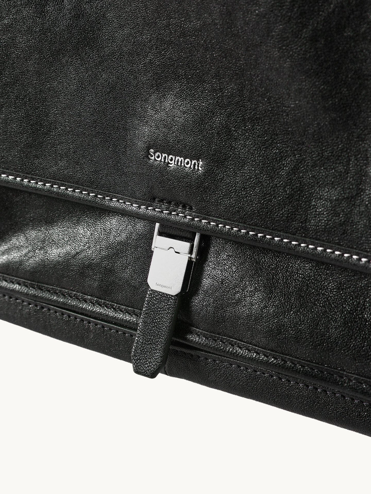 Songmont Small Shan Messenger Bag Onyx - close-up of the logo, contrast stitching and buckle tab