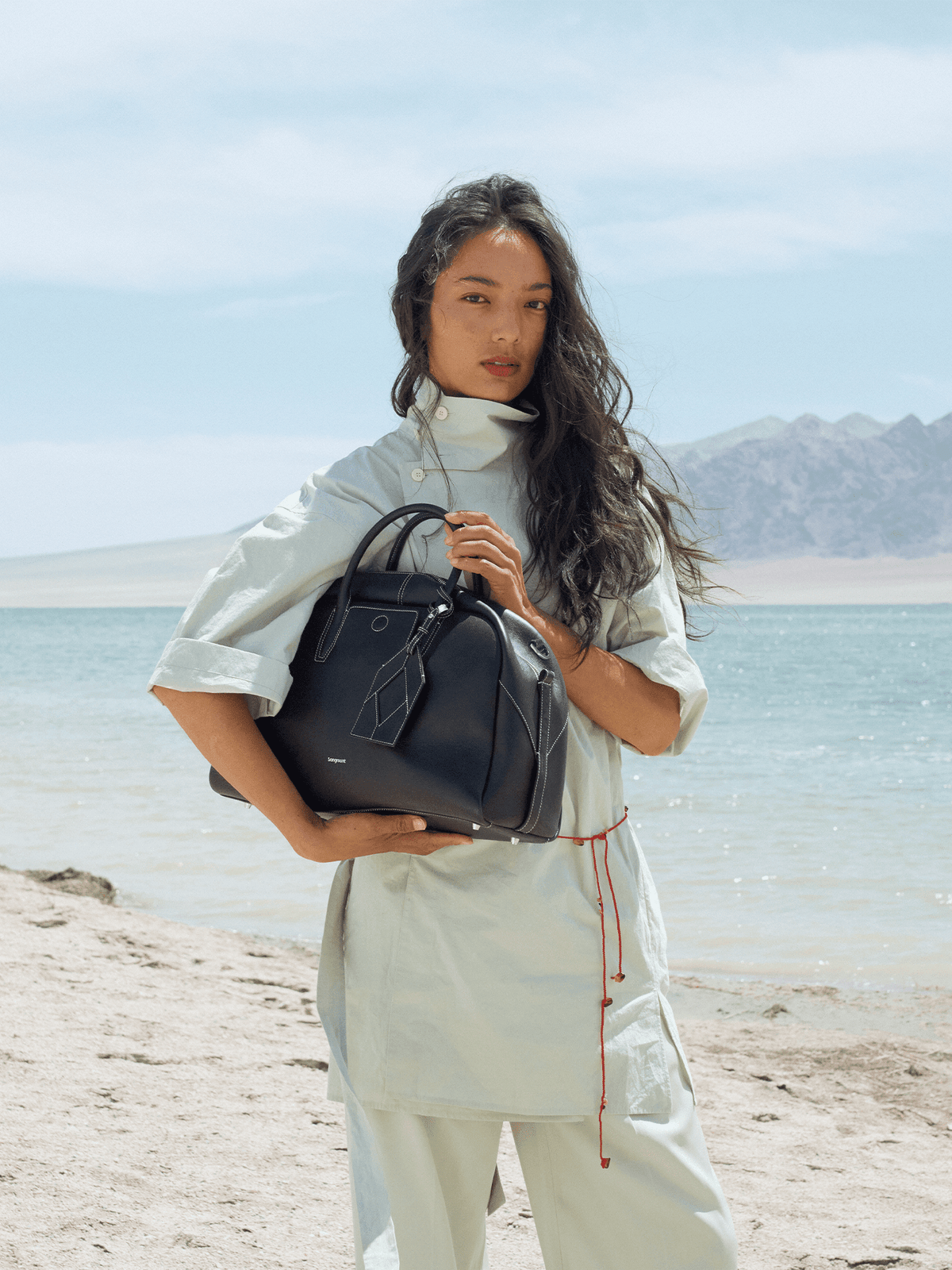 Songmont Large Yore Bowling Bag Ebony - held in both hands on a beach