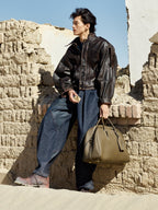 Songmont Large Yore Bowling Bag Moss - carried by hand against a sand-coloured wall