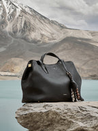 Songmont Large Yore Tote Bag Onyx - on a rock by a mountain lake with a beaded charm