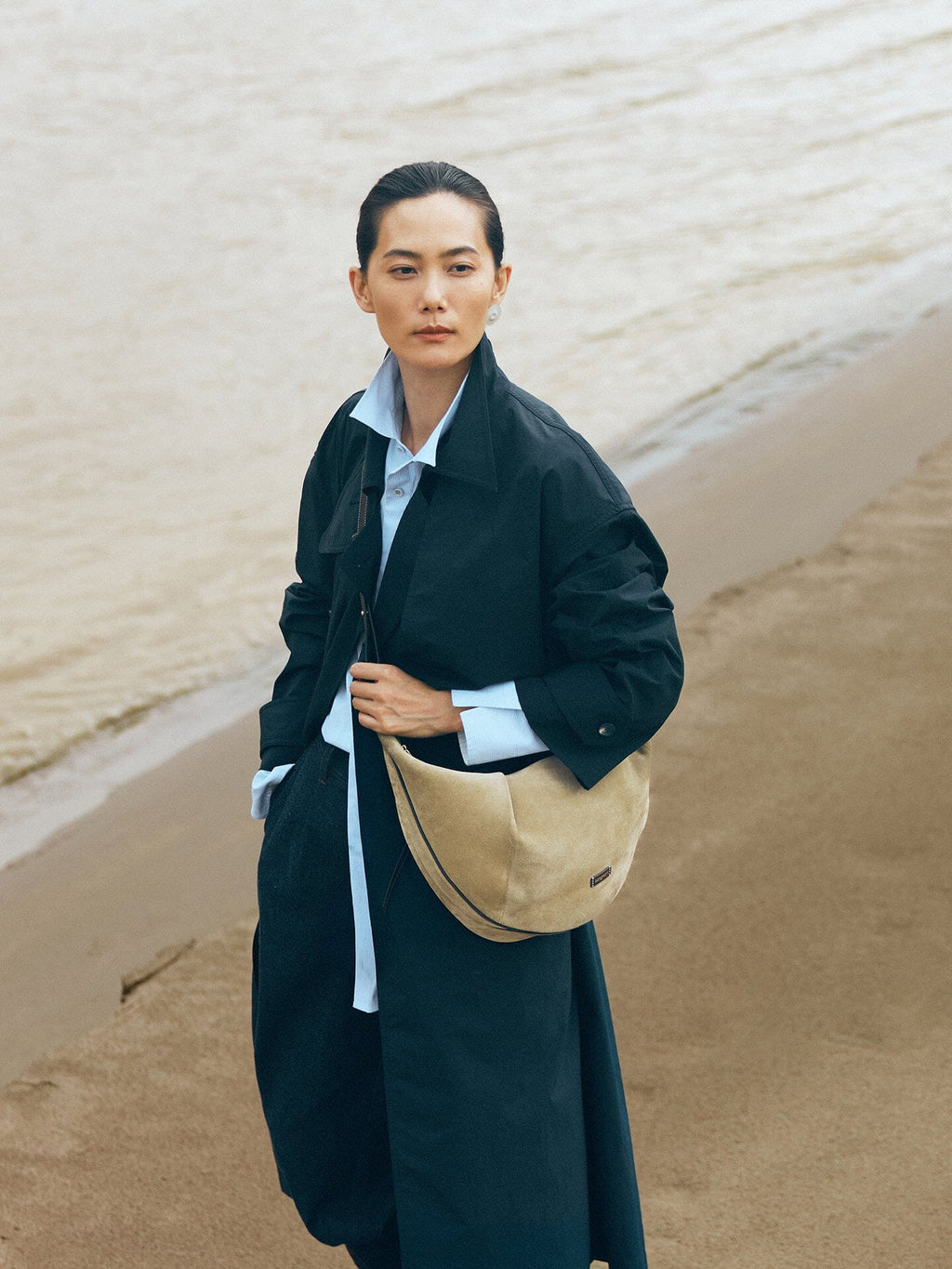 Songmont Large Luna Hobo Bag Dune Suede - worn cross-body over a dark coat on a beach