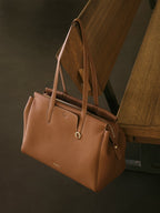 Songmont Medium Yore Duffle Bag Golden Brown - hanging by its handles against dark wood