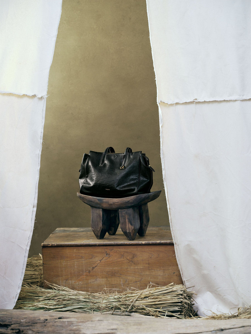 Songmont Medium Yore Duffle Bag Onyx - styled on a carved wooden stool