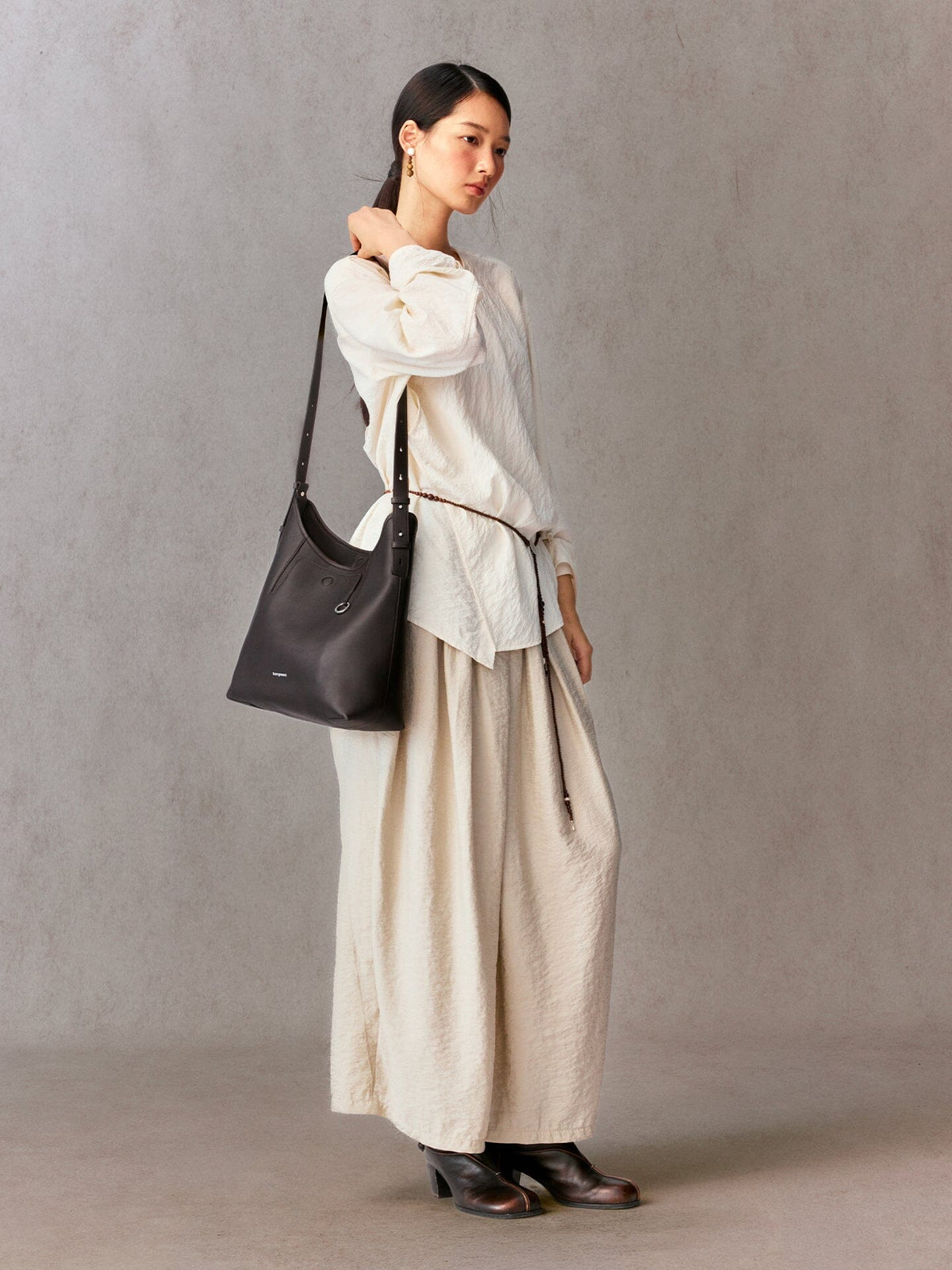 Songmont Medium Yore Shoulder Bag Ebony - worn over the shoulder with a cream outfit