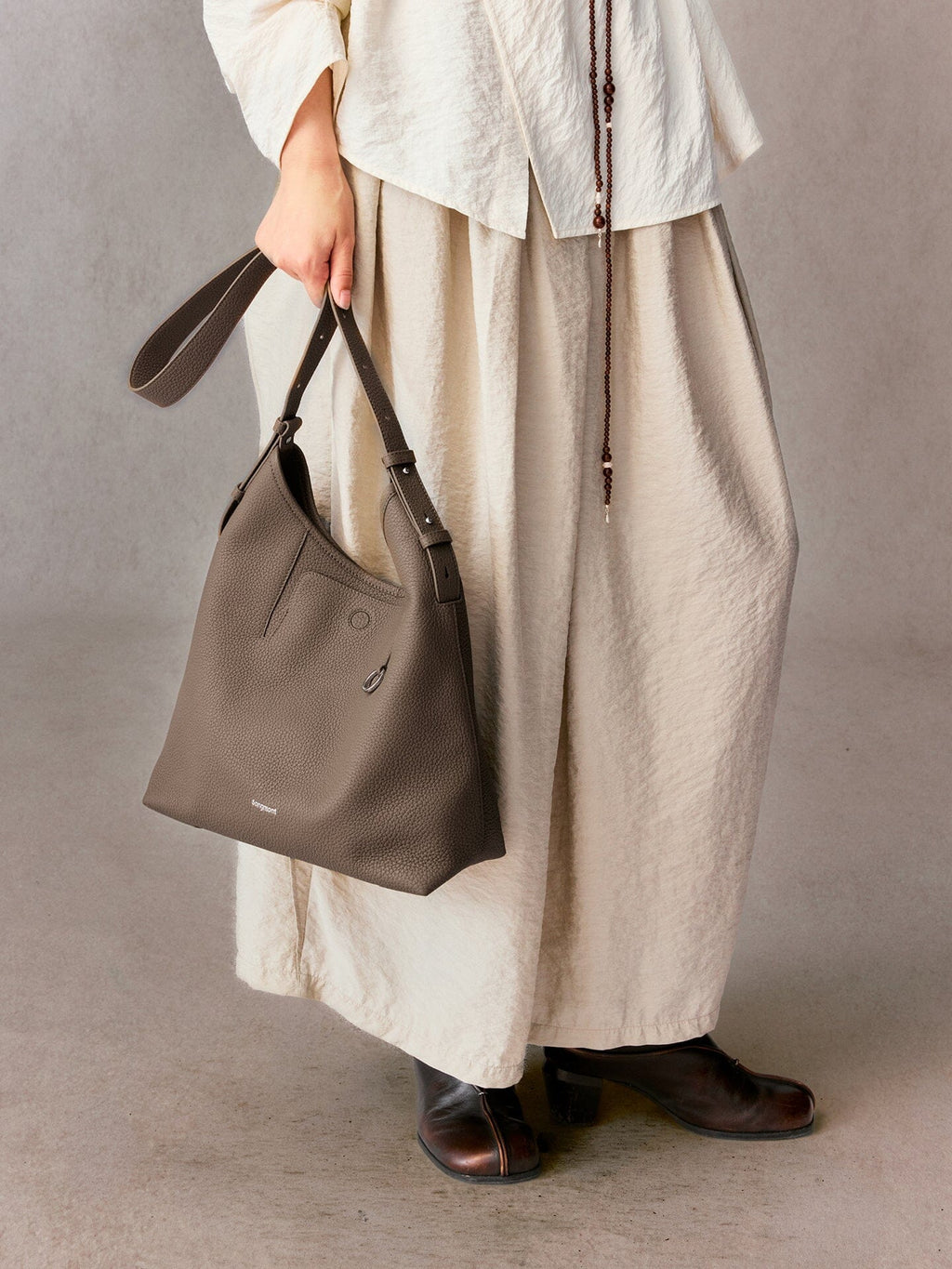 Songmont Medium Yore Shoulder Bag Stone - carried by the strap with a cream skirt