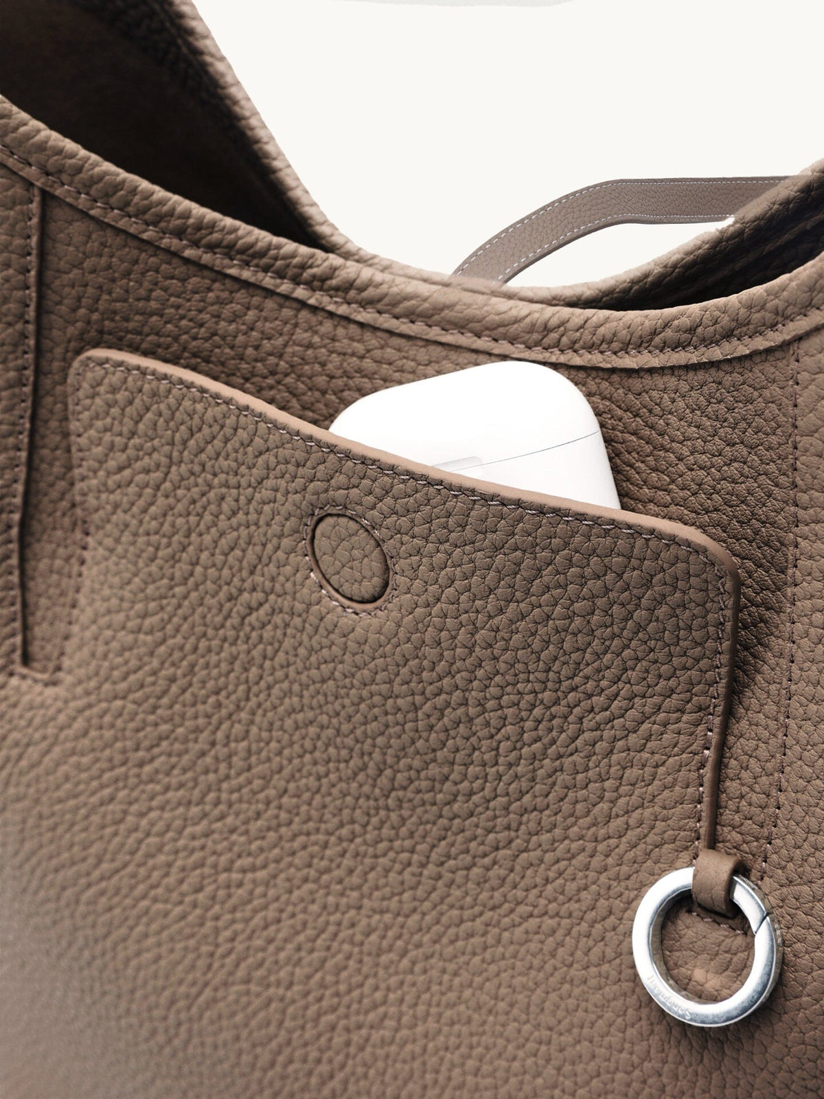 Songmont Medium Yore Shoulder Bag Stone - front pocket open with an AirPods case inside