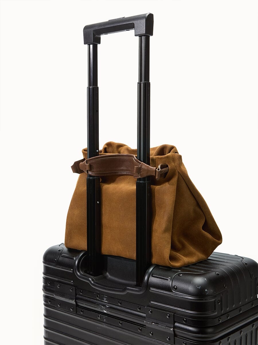 Songmont Small Gather Bag Ochre Suede - on a suitcase handle