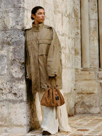 Songmont Small Gather Bag Ochre Suede - carried by hand against a stone wall