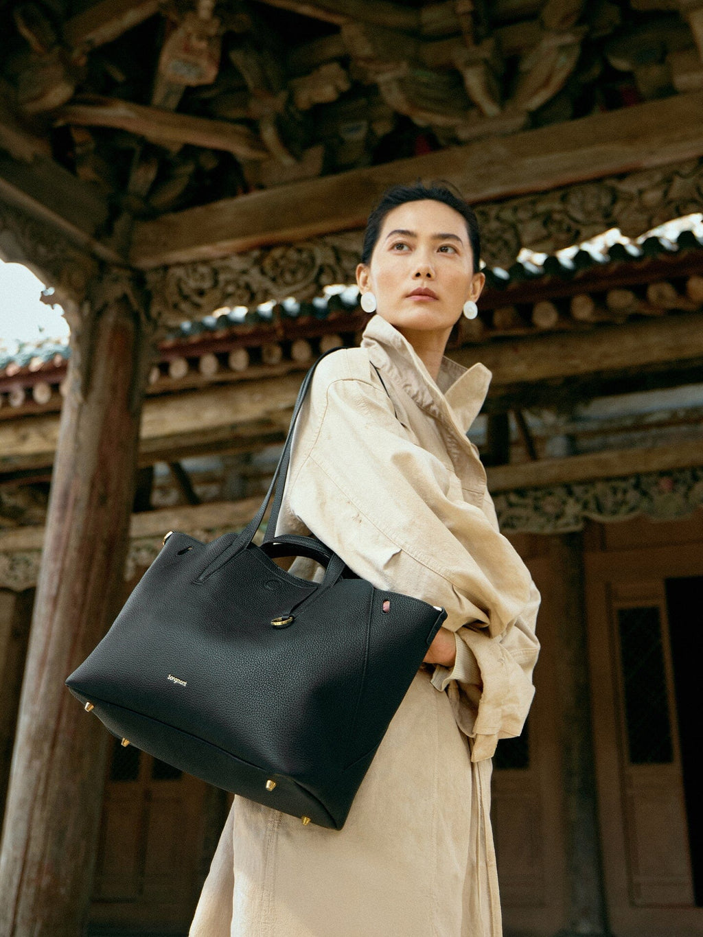 Songmont Small Yore Tote Bag Onyx - worn on the shoulder beneath carved timber eaves