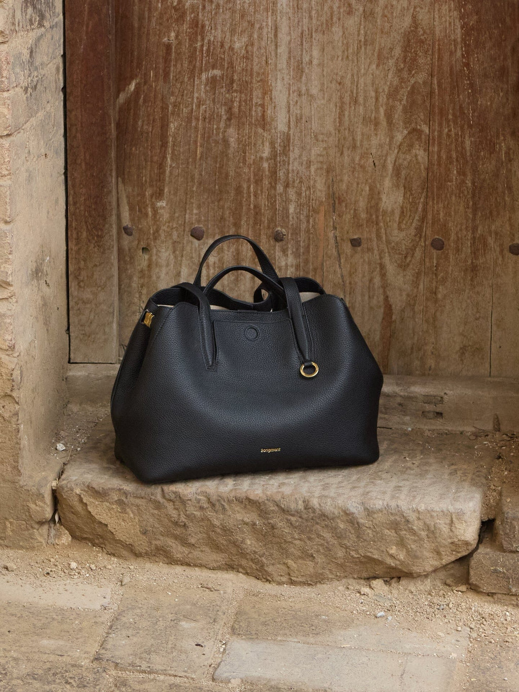 Songmont Small Yore Tote Bag Onyx - on a stone step before a weathered timber door