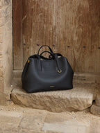 Songmont Small Yore Tote Bag Onyx - on a stone step before a weathered timber door