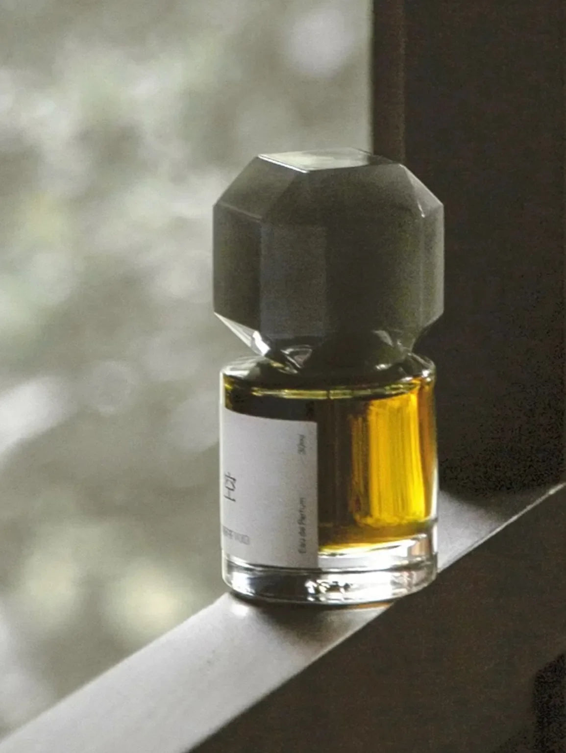 TO SUMMER Void Eau de Parfum bottle glowing amber in window light