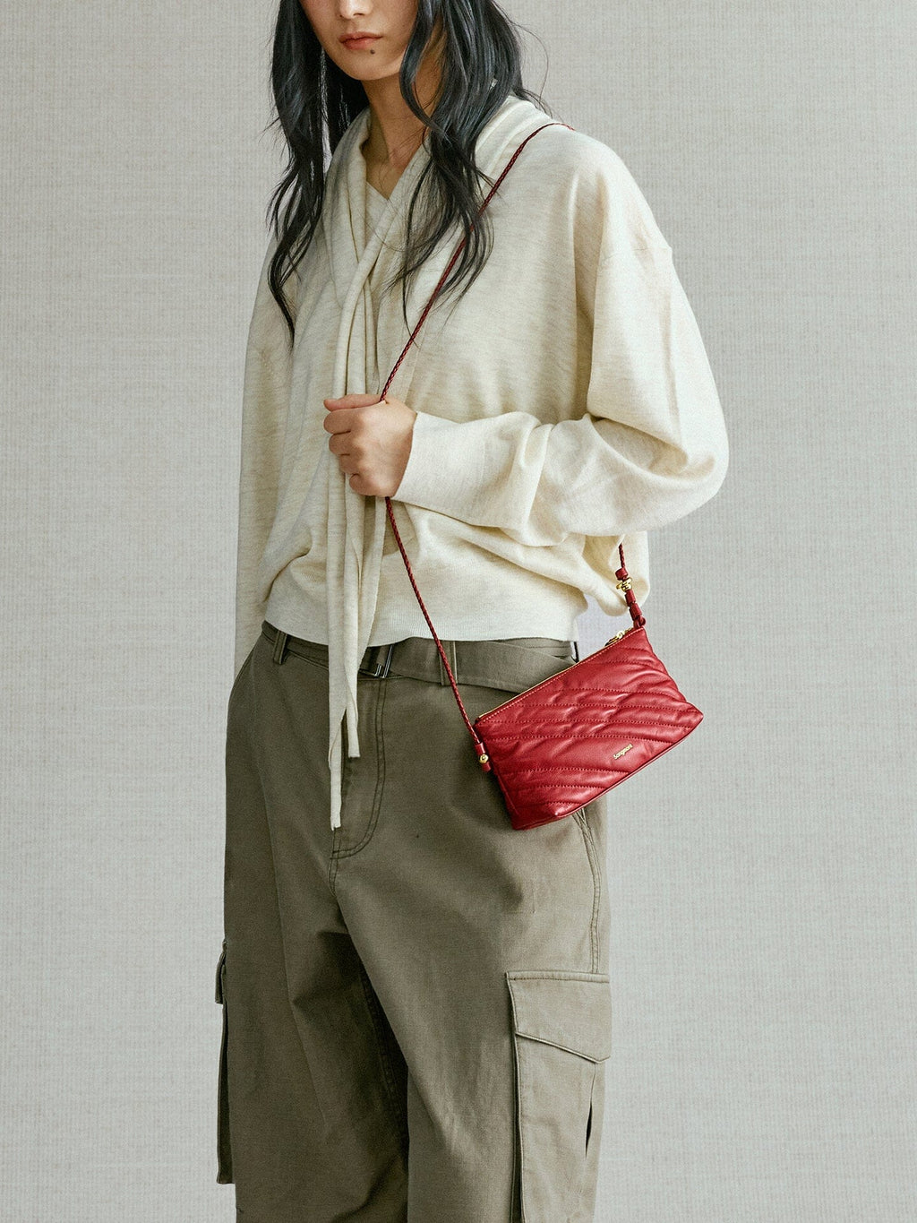 Songmont Winding Underarm Bag Lucky Red - held across the body with cream knit and cargo trousers