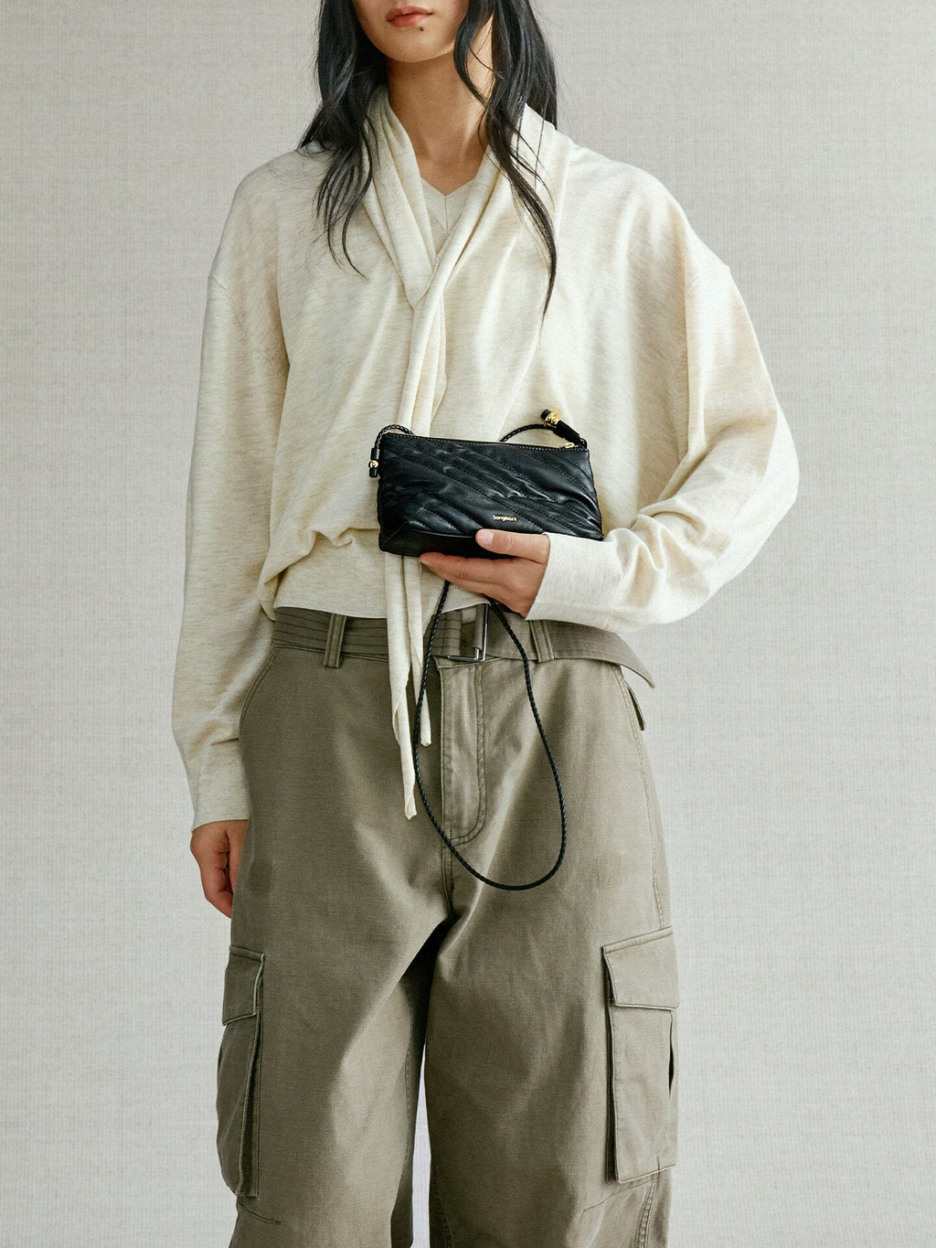 Songmont Winding Underarm Bag Onyx - held in hand with cream knit and cargo trousers