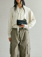 Songmont Winding Underarm Bag Onyx - held in hand with cream knit and cargo trousers