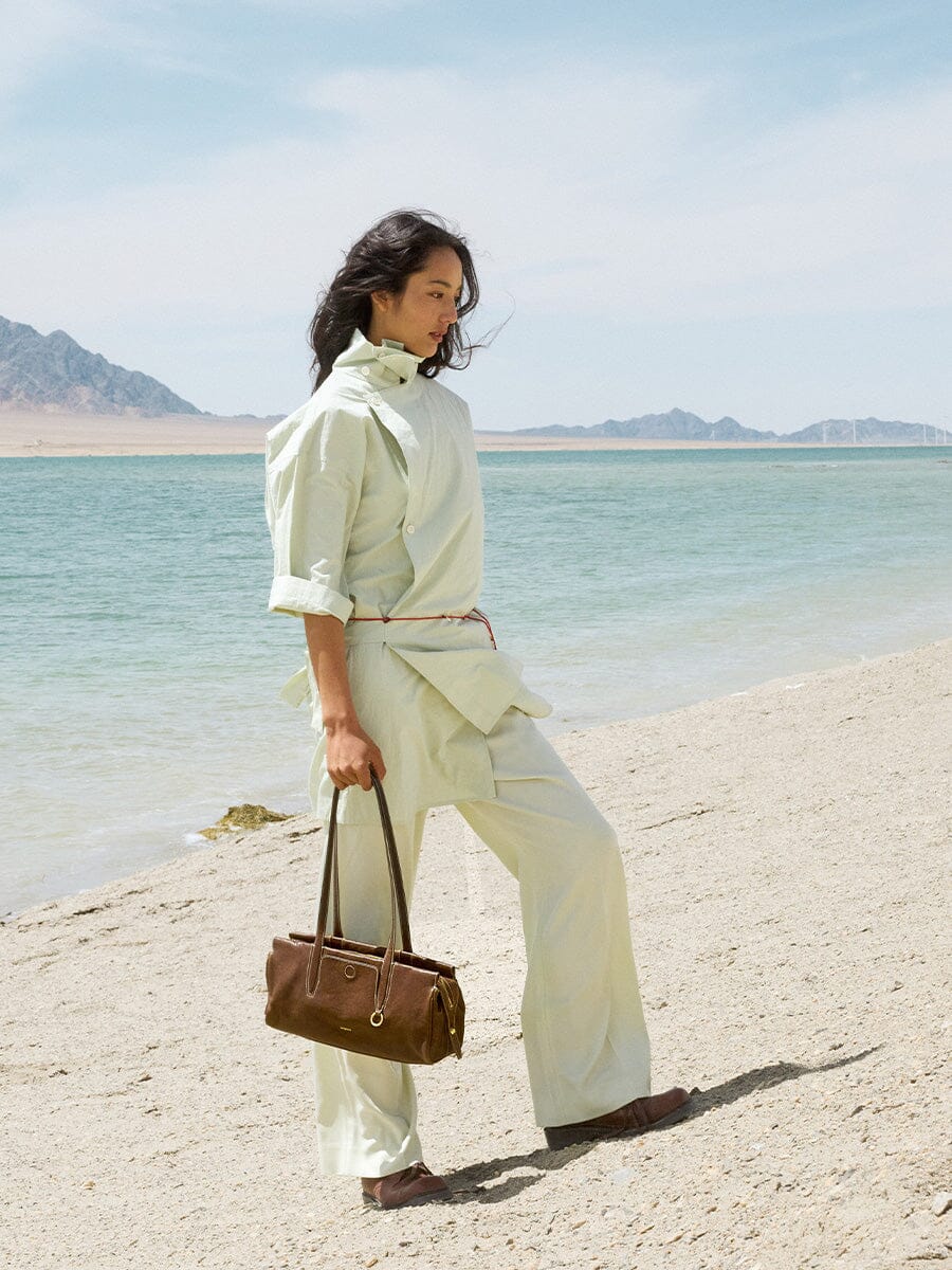 Songmont Yore Baguette Bag Sandal held by hand on the beach