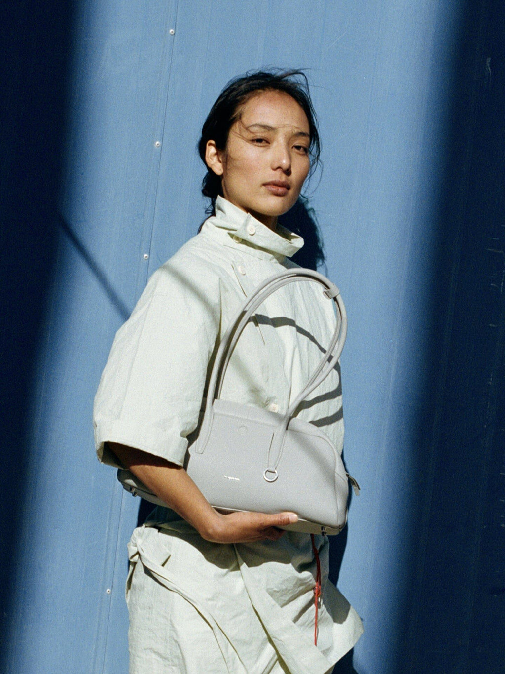 Songmont Yore Toast Bag Celeste - carried in the crook of the arm against a blue wall
