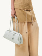 Songmont Yore Toast Bag Celeste - held by the handles beside a linen outfit