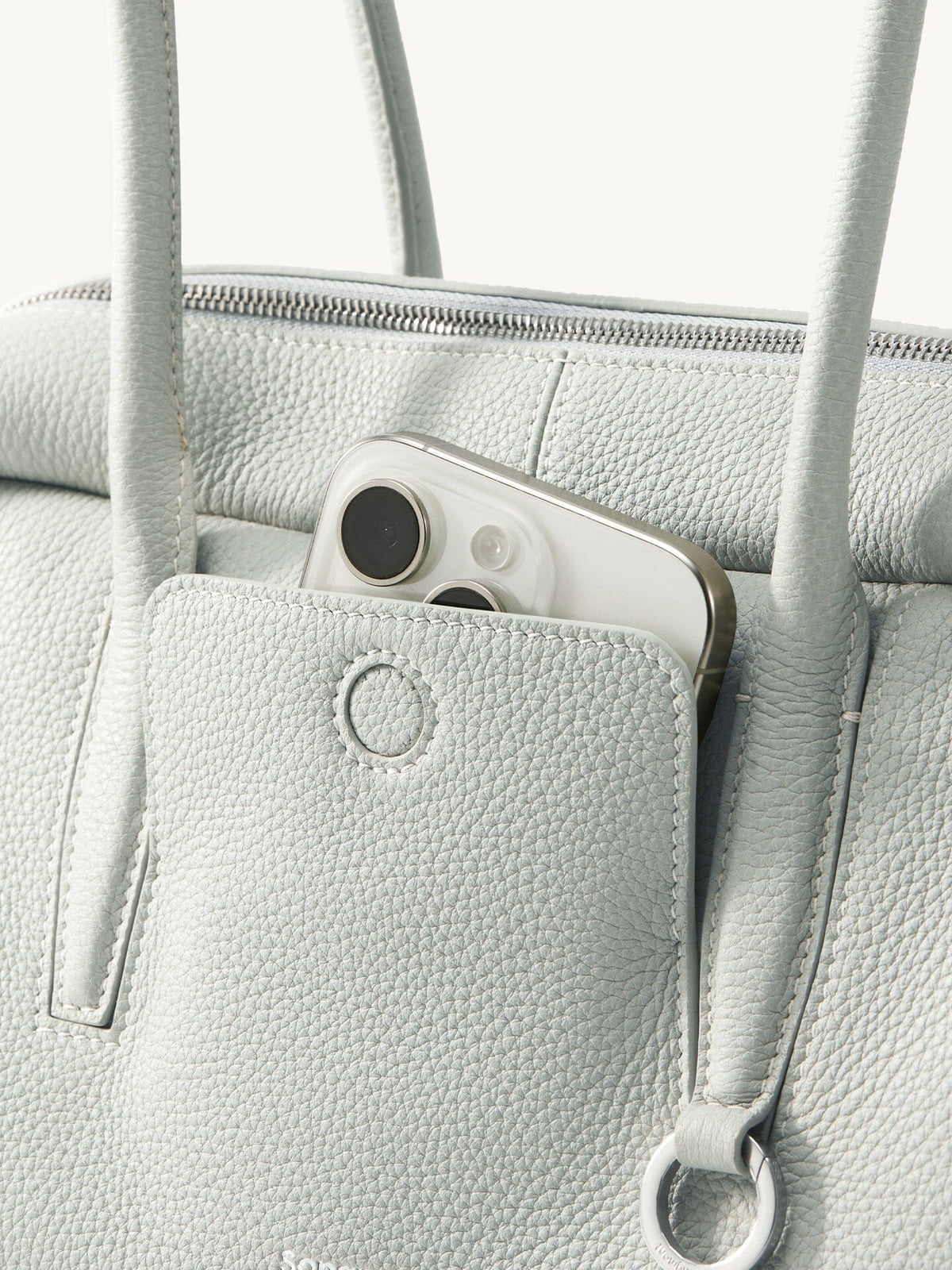 Songmont Yore Toast Bag Celeste - front slip pocket holding a phone, metal ring detail