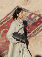 Songmont Yore Toast Bag Ebony - held under the arm against a patterned rug